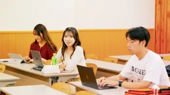 ノートパソコンを用いて授業を受けている3名の大学生